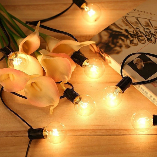 String lights with glowing bulbs draped over pink flowers on a wooden surface.